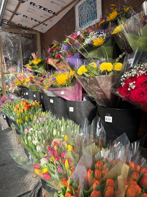 A variety of fresh flower bouquets displayed in black buckets inside a flower shop, showcasing an array of colorful arrangements. Prominent blooms include yellow daffodils, pink and orange tulips, pur