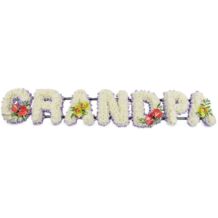 A dignified, personalised sympathy tribute in the photograph spells out "GRANDPA" in bold, three-dimensional letters that appear to float gently against a bright white background. Crafted by a skilled florist, each individual character is built on a sturdy frame then completely covered with small white chrysanthemums, positioned so closely that the eye sees an unbroken field of soft texture and calm colour. The chrysanthemums' petals form tiny, layered rosettes, suggesting comfort and tranquillity, an appropriate choice for funeral flowers travelling to services in Brunswick Park or nearby Barnet crematoria. At the base of each letter, a band of pale lavender ribbon peeps out, tracking the contours and giving a faint halo of colour that separates the snowy petals from the supporting structure beneath. Linking the letters from behind are slim dark green bars, practical yet almost invisible from the front, ensuring the tribute remains straight and secure during transport and display. Carefully integrated among the white blooms are four accent clusters of colour, placed to balance the design. On the "G" and the "D", rich red anthuriums stand out, their high-gloss, heart-shaped spathes and upright yellow spadices framed by polished green leaves and a hint of purple fillers, conveying deep affection and remembrance. On the first and last "A", a gentler note is struck by sprays of yellow-green orchids, their refined starry flowers and arching stems bringing lightness and hope. Overall, the arrangement reads as a heartfelt farewell to a much-loved grandfather, a custom funeral tribute that might be laid lovingly beside the coffin or near the altar, offering a tangible expression of respect and family devotion when words alone feel inadequate.